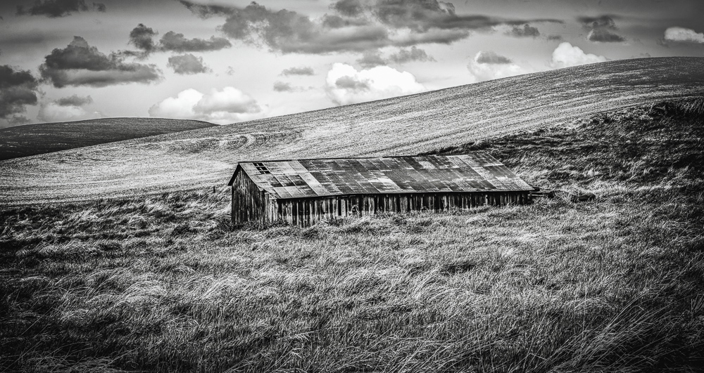 A black and White image of a spooky old abandoned barn under threatening weather clouds in Eastern Washington