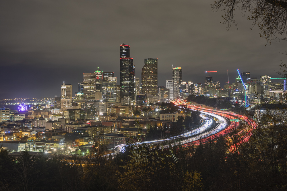 Nightime view of the Seattle Skyline with traffic on I-5.  The Seattle Great Wheel is to the far left.